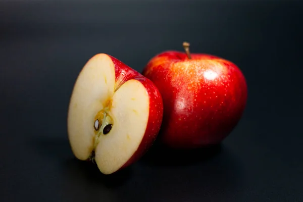 Ekranın ortasında kırmızı sulu bir elma ve aynı kenarın yarısı var. Koyu arkaplan. — Stok fotoğraf