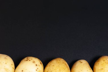 Ekranda koyu bir arka plan var. En altta bir sıra çiğ patates yumrusu var..