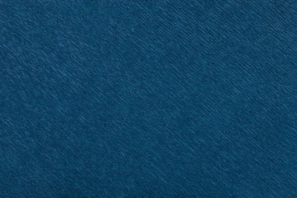 Textural of navy blue background of wavy corrugated paper, closeup. Structure of wrinkled crepe dark denim cardboard macro.