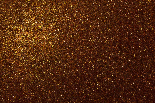 Dark golden sparkling background from small sequins, closeup. Brilliant shiny orange backdrop from textile. Shimmer bronze paper