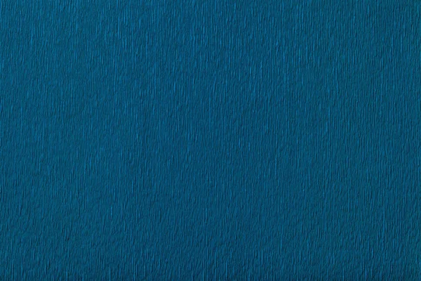 Textural of navy blue background of wavy corrugated paper, closeup. Structure of wrinkled crepe dark denim cardboard macro.