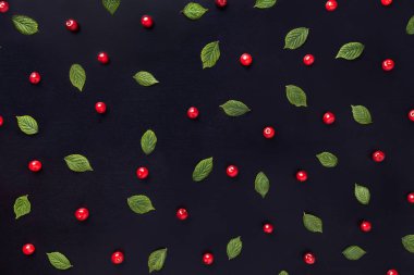 Siyah ahşap arka plan üzerinde yeşil yaprakları ile kırmızı kiraz desen, düz yatıyordu.