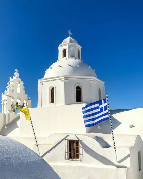 Edifício de templo branco com uma torre sineira na ilha Santorini. Bandeira nacional de Greece . — Fotografia de Stock