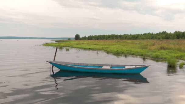 Old blue wooden boat anchored off the coast of the bay sways on calm waves. — Stock Video