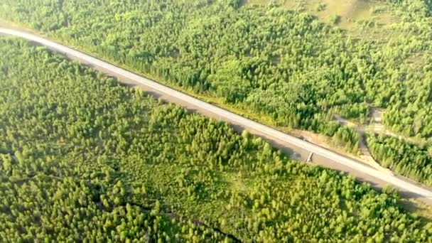 Vuelo aéreo sobre un camino rural vacío sin un coche entre bosques en un día soleado. — Vídeos de Stock