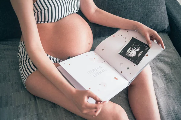 Těhotná žena s dětskou knihou a obrázkem sonogram — Stock fotografie