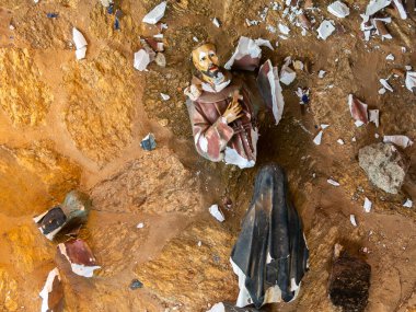 Broken vandalized plaster catholic plaster statues in the ground clipart