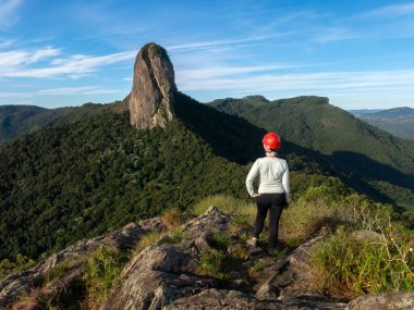 Kask takan bir kız dağın zirvesinden kayalık bir dağa bakıyor - Pedra do Bau