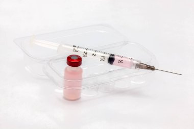 Bir plastik aşı şişesi, on aşı şişesi ve bir şırınga dolusu sıvı için şeffaf plastik bir kutunun içinde.