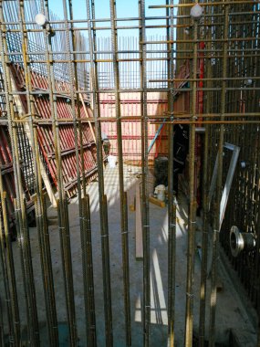 Bir sürü iskelesi ve metal parmaklıkları olan bir inşaat alanı. İşçiler bir yapı inşa etmekle meşgulken, sahne gergin ve ciddi.