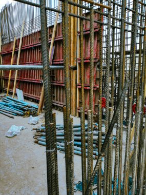 Kırmızı duvara yaslanmış iki mavi metal direk. Direkler duvarın tepesine yerleştirilmiş ve duvar kırmızı ve beyaz malzemelerden yapılmış. Olay yeri bir inşaat alanı gibi görünüyor.