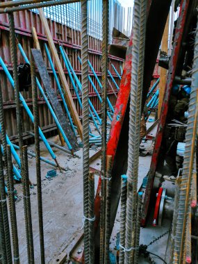 Kırmızı duvara yaslanmış iki mavi metal direk. Direkler duvarın tepesine yerleştirilmiş ve duvar kırmızı ve beyaz malzemelerden yapılmış. Olay yeri bir inşaat alanı gibi görünüyor.