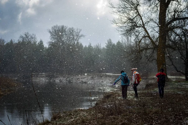 A group of hikers walks along the river during the first snowfall
