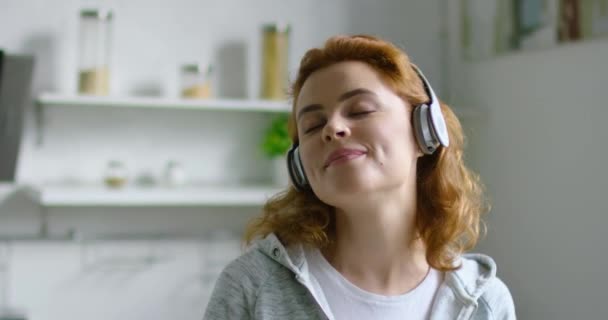 Mujer joven está escuchando música en auriculares inalámbricos en casa — Vídeo de stock
