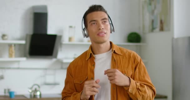 Hombre hispano está escuchando música en auriculares inalámbricos en casa — Vídeos de Stock