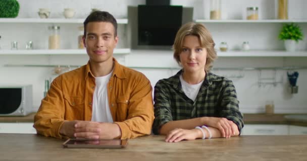 Portret van jonge Latijnse man en blanke vrouw zittend aan tafel in de keuken — Stockvideo