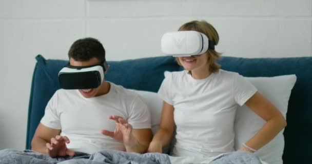 Pareja joven tumbada en la cama, viendo 360 videos en auriculares de realidad virtual — Vídeos de Stock