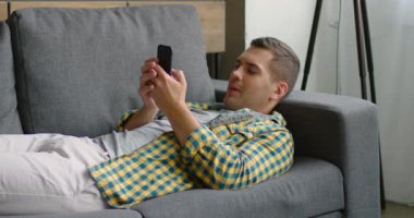 Yakışıklı adam kanepede yatan, cep telefonu tarama