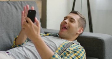 Mutlu adam bir kanepede yatan ve bir görüntülü sohbet sahip