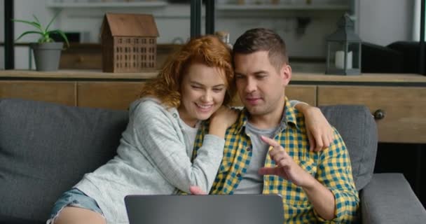 Νεαρό ζευγάρι χαλαρωτικό σε έναν καναπέ, περιήγηση στο φορητό υπολογιστή — Αρχείο Βίντεο