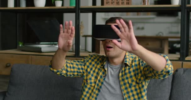 Молодий чоловік сидить на дивані у гарнітурі віртуальної реальності — стокове відео