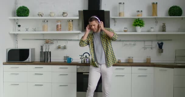 Joven hombre atractivo está bailando y escuchando música en su cocina — Vídeos de Stock