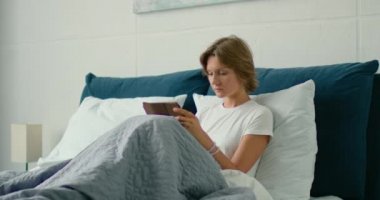 Genç kadın sabah yatakta yatan, tablet bilgisayar kullanarak