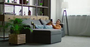İspanyol adam kanepede yatıyor, akıllı telefonda geziniyor