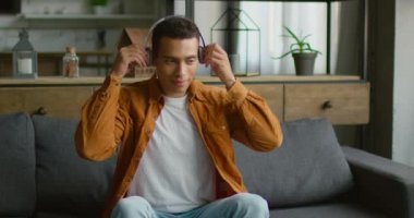 Genç İspanyol adam kablosuz kulaklık takıyor, kanepede oturuyor, gadget kullanıyor