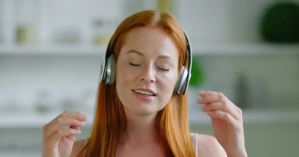 Jonge mooie vrouw luistert muziek in draadloze headset thuis — Stockvideo