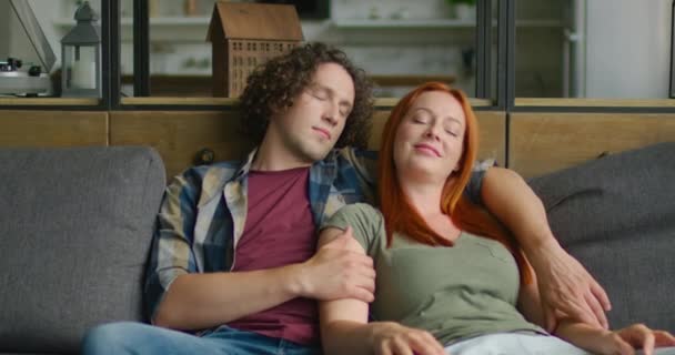 Νεαρό ζευγάρι σε ρομαντική διάθεση είναι χαλαρωτικό με κλειστά μάτια στον καναπέ στο σπίτι — Αρχείο Βίντεο