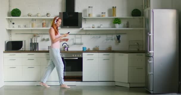 Young woman in positive mood is dancing and listening music kitchen — Stock Video
