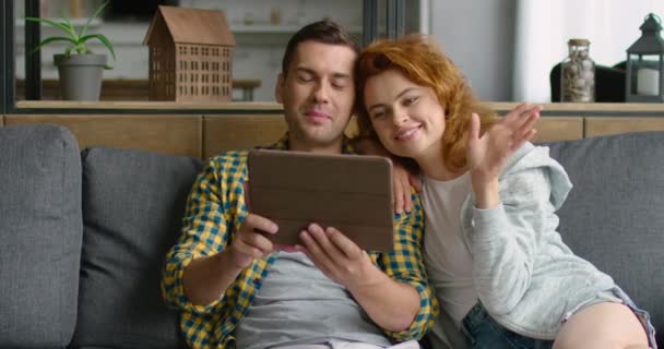 Young couple has a video chat on tablet computer, sitting on sofa — Stock Video