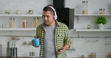 Genç çekici adam kablosuz kulaklık giyiyor, mutfağında müzik dinliyor