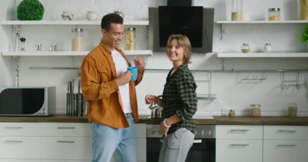 Jóvenes de raza mixta pareja está bailando en la cocina, disfrutando de la mañana — Vídeos de Stock