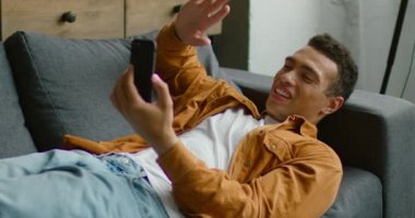 İspanyol adam kanepede yatıyor, akıllı telefon üzerinden görüntülü sohbet yapıyor