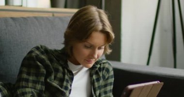 Genç kadın kanepede yatıyor, tablet bilgisayar kullanıyor, yakından