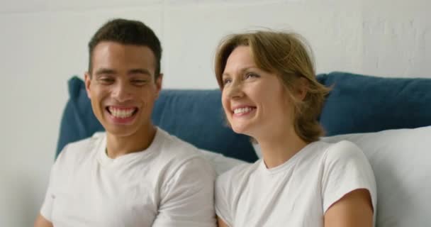 Jovem casal misto relaxando na cama, conversando uns com os outros — Vídeo de Stock