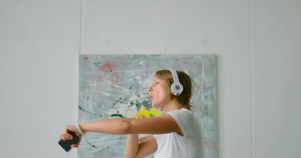 Mujer joven está bailando en la cama, con auriculares inalámbricos, de cerca — Vídeos de Stock