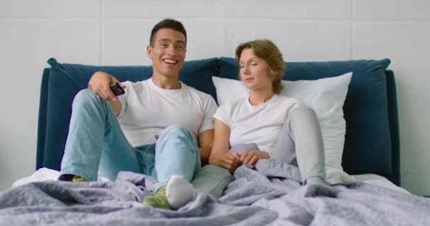 Молодая смешанная пара смотрит телевизор в спальне, женщине скучно — стоковое видео