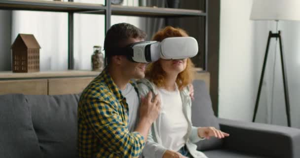 Pareja reacciona emocionalmente en imágenes de realidad virtual, sentado en el sofá en casa — Vídeos de Stock