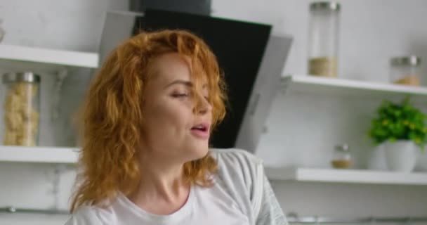 Gelukkige jonge vrouw met rood haar is dansen in de keuken, close-up — Stockvideo