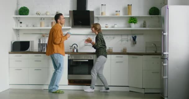 Jeune couple mixte s'amuse dans la cuisine, profitant de leur week-end matin — Video