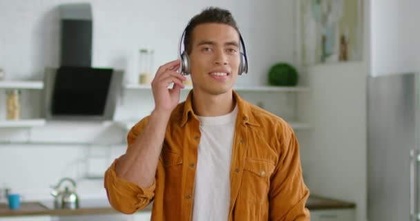 Młody łaciński człowiek cieszy się pauza muzyka, noszenie bezprzewodowego zestawu słuchawkowego w kuchni — Wideo stockowe