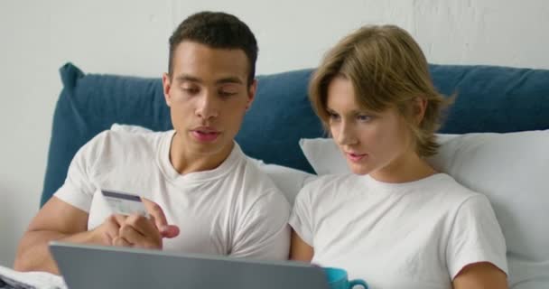 Jeune couple mixte fait un achat en ligne, couché dans un lit — Video