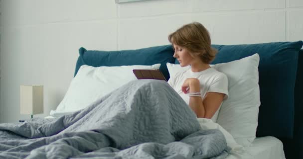 Junge Frau liegt im Bett, liest, spricht auf ihrem Smartphone — Stockvideo