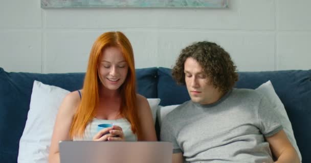 Jong paar is blij als gevolg van succesvolle online aankoop, liggend in bed — Stockvideo