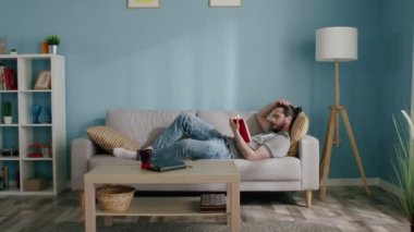 Adam oturma odasında kitap okuyor.