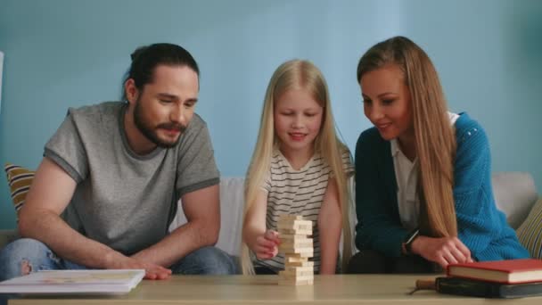 Blond meisje speelt Jenga met mama en papa en verliest — Stockvideo