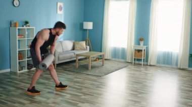 Genç adam oturma odasında fitness matı yayıyor.